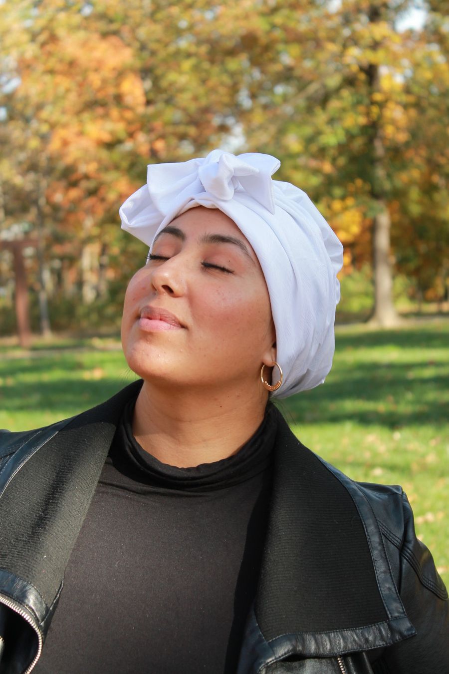 Natalie outdoors in autumn, eyes closed, wearing a white headwrap with a bow