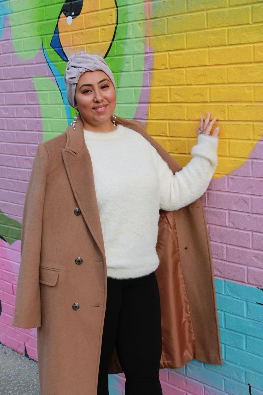 Natalie, founder of Scarves for Healing, smiling in a blush pre-tied headwrap and camel coat