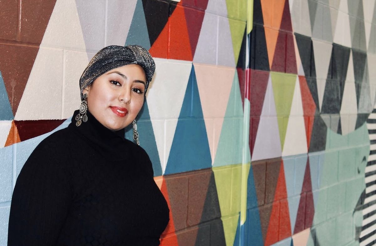 Natalie in a shimmering charcoal headwrap in front of a geometric mural